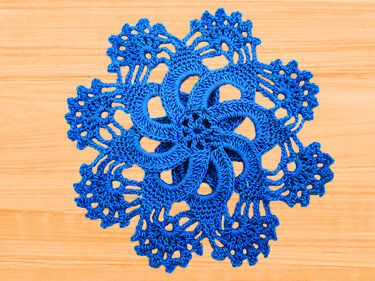 Blue crocheted round doily-style coaster with lacy floral pattern on wooden table