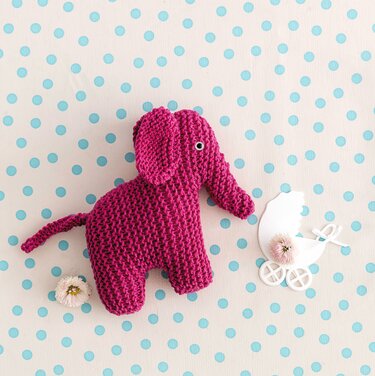 Detailaufnahme eines gestrickten fuchsienfarbenen Elefanten mit sichtbarer kraus‑rechts Maschenstruktur auf gepunktetem Untergrund