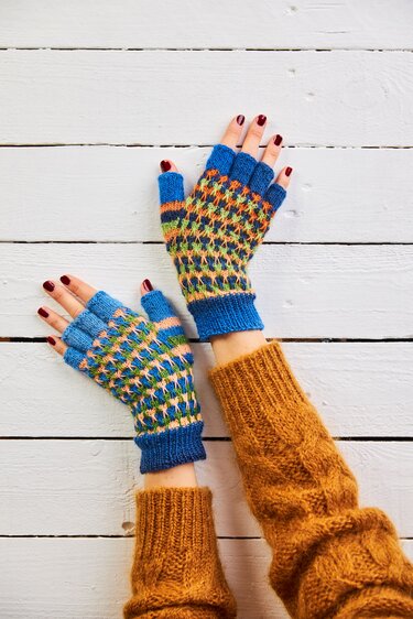Hände mit bunten, fingerlosen Strickhandschuhen auf weißem Holzuntergrund