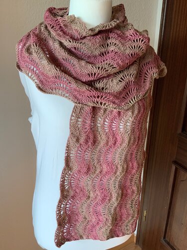 Zweifarbiger gehäkelter Schal in Rosa und Beige mit durchbrochenem Wellenmuster auf weißer Kleiderbüste.