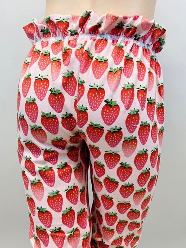 Rückansicht einer Kinderhose mit rotem Erdbeermuster auf hellrosa Stoff und elastischem, gerafftem Rüschenbund.