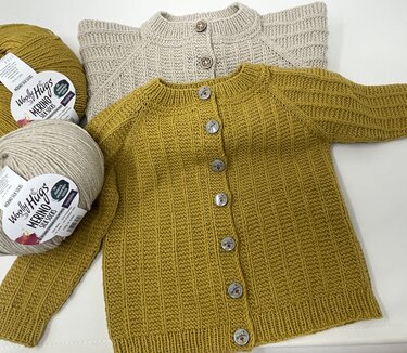 Zwei gestrickte Babyjacken in Senfgelb und Beige mit Garnknäueln