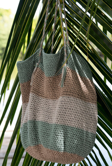 Gestreifte gehäkelte Tasche in Grün und Beige, hängend an einem Palmenblatt