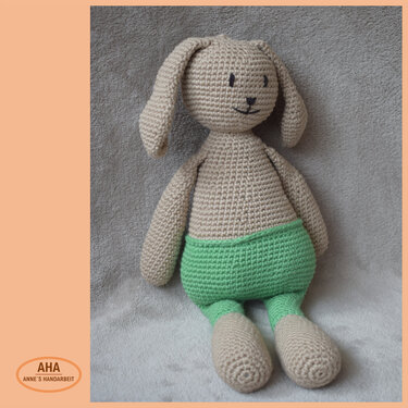 Gehäkelter Amigurumi-Hase beige mit grüner Hose, sitzend