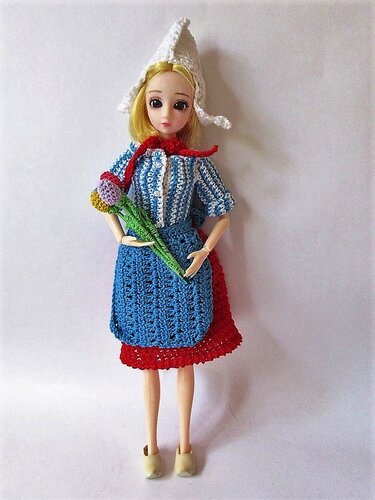 Ankleidepuppe mit gehäkeltem Trachten-Outfit: blau-weiß gestreiftes Oberteil, blaue Schürze, roter Rock, weiße Haube und gehäkelte Blume.