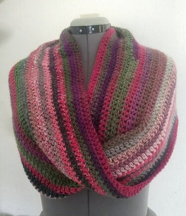 Mehrfarbiger gehäkelter Loop-Schal auf einer Schneiderpuppe in Rosa, Lila und Olivgrün.