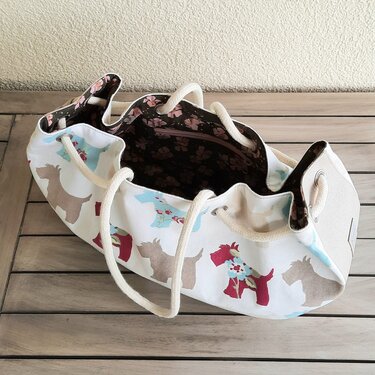 weiße Stofftasche mit bunten Hundesilhouetten, Kordelgriffen und dunklem Innenfutter mit Reißverschlussfach