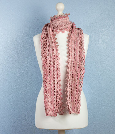 Handgehäkelter Schal in Rosatönen mit Lochmuster und gewellter Kante auf einer Schneiderpuppe.