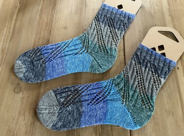 Paar handgestrickter Socken in Blau-Grün mit diagonalem Ajourmuster auf Holzuntergrund