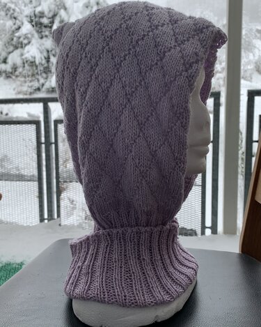 Helllila gestrickte Kapuze mit Rautenmuster und hohem Rippenkragen auf Schaufensterpuppe vor verschneitem Balkon