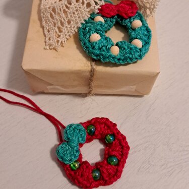 Zwei gehäkelte Mini-Weihnachtskränze in Türkis und Rot mit Holzperlen und Schleifen, einer auf Geschenk, einer als Anhänger
