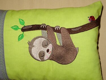 Gesticktes schlafendes Faultier am Ast mit Marienkäfer auf hellgrünem Stoff