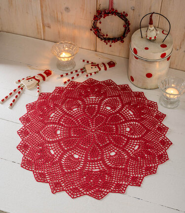 Rotes rundes Häkeldeckchen auf weißem Tisch mit Kerzen und Weihnachtsdekoration