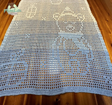 Gehäkelter Tischläufer mit blau‑weißem Farbverlauf und Lochmuster auf Holztisch.