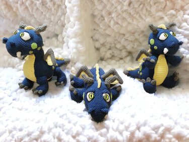 Three crocheted blue dragons with yellow bellies and grey horns shown from front, side and top head views on a soft white background