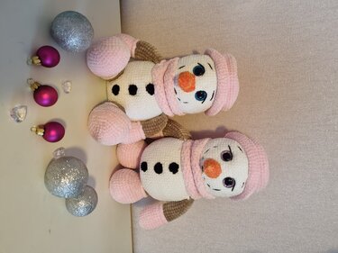 Zwei Amigurumi-Schneemänner mit rosa Mützen und festlicher Dekoration