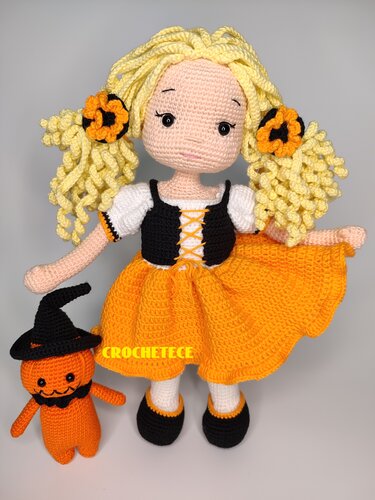 Crochet amigurumi doll with orange skirt, curly blonde pigtails, and small pumpkin plush in witch hat