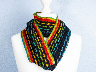 Schwarzer gestrickter Loop-Schal mit roten, gelben, grünen und blauen Streifen auf weißer Schaufensterpuppe
