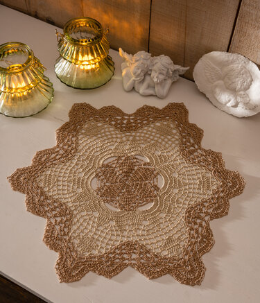 Handgehäkeltes sternförmiges Deckchen in Braun- und Goldtönen auf hellem Tisch, dekoriert mit goldenen Laternen und Engelsfiguren.