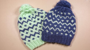 Zwei gestrickte Bommelmützen in Mintgrün und Dunkelblau mit zweifarbigem Jacquardmuster