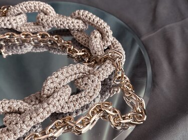 Close-up of beige crocheted chain-link loops intertwined with a gold-tone metal chain