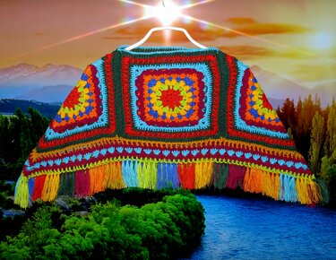 Bunter handgehäkelter Kinderponcho aus Granny Squares mit mehrfarbigen Fransen, aufgehängt vor einer Landschaft.