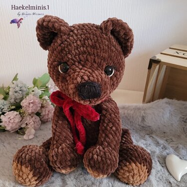 Sitzender gehäkelter Amigurumi-Teddybär in Braun mit roter Schleife