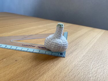 Gehäkelte Mini-Knoblauchknolle neben Geodreieck zur Größeneinschätzung