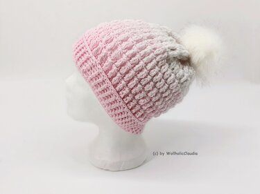 Rosa gehäkelte Beanie mit Strukturmuster und weißem Bommel auf weißer Schaufensterbüste