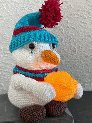 Gehäkelter Schneemann mit türkis‑roter Mütze, Schal und orangefarbener Leuchte