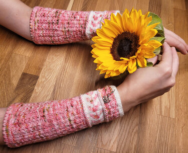 Gestrickte rosa Armstulpen an Armen, eine Hand hält eine Sonnenblume