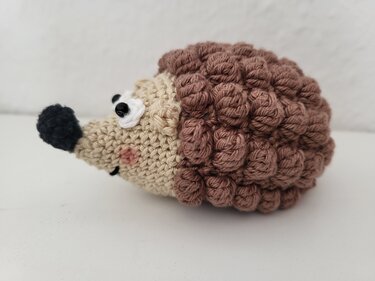 Gehäkelter Amigurumi-Igel mit beigem Kopf, schwarzer Nase und braunem Noppenrücken auf hellem Hintergrund