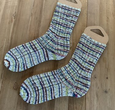 Zwei gestrickte mehrfarbige Socken mit Karo- und Streifenmuster auf Pappsockenformen auf hellem Holztisch.