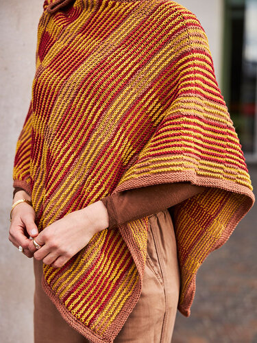 Gestrickter Damenponcho mit gelb-roten Streifen und Terrakotta-Saum über braunem Oberteil