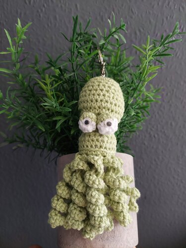 Hellgrüner gehäkelter Amigurumi-Oktopus-Schlüsselanhänger vor einer Zimmerpflanze