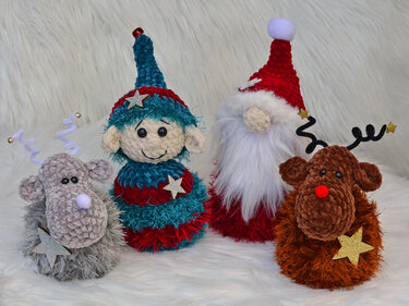 Nahaufnahme von vier gehäkelten Weihnachtsfiguren (zwei Rentiere, ein Elf, ein Wichtel) auf flauschigem Untergrund.