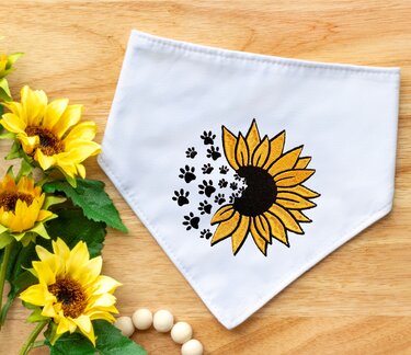 Detailliertes Stickmotiv: gelbe Sonnenblume mit schwarzen Pfotenabdrücken auf weißem Stoff