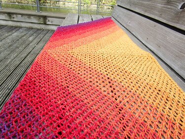 Triangle ombr
shawl in red to yellow gradient draped flat on a wooden bench showing lace texture.