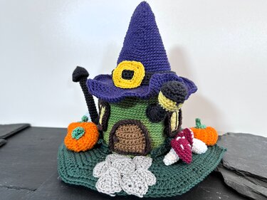Gehäkeltes grünes Hexenhaus mit violettem Hut, Kürbissen, Pilzen und grauen Bodenmotiven