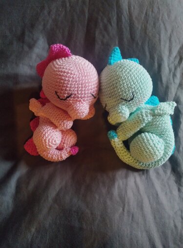 Gehäkelte Amigurumi‑Drachen in zusammengerollter Schlafposition, rosa und mint