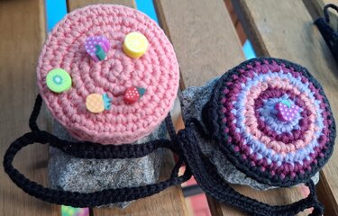 Zwei runde gehäkelte Täschchen in Rosa und Lila mit Fruchtknöpfen und schwarzem Trageband