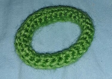 Ovaler grüner gehäkelter Ring aus Garn auf hellblauem Stoff
