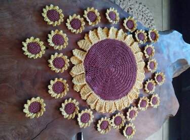Gehäkeltes rundes Sonnenblumen-Tischset mit vielen kleinen Sonnenblumen-Applikationen auf dunklem Holz