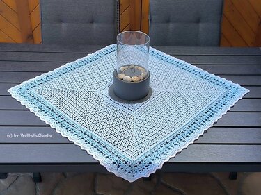 Quadratisches gehäkeltes Deckchen in Hellblau und Weiß auf dunklem Tisch mit Windlicht