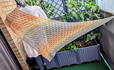 Crocheted triangle shawl in beige-to-peach-to-grey gradient draped over a chair on a balcony