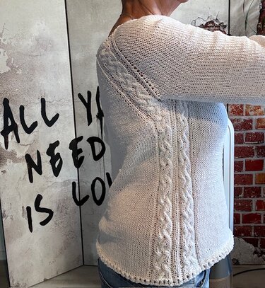 Seitliche Ansicht eines hellen, gestrickten Damenpullovers mit Zopfmustern an Seiten und Schultern.