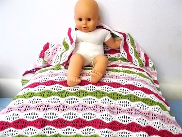Gehäkelte Babydecke mit Wellenmuster in Rosa, Grün und Weiß, Babypuppe liegt darauf