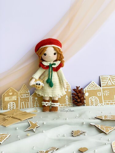Crocheted amigurumi girl in red beret and cream dress holding a tiny white bird among paper village houses