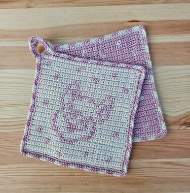 Zwei quadratische, gehäkelte Topflappen in Rosa und Creme, einer mit Hasenmotiv und Aufhängeschlaufe
