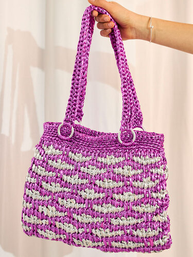 Hand hält eine violett-silberne Henkeltasche mit dichtem Häkelmuster.